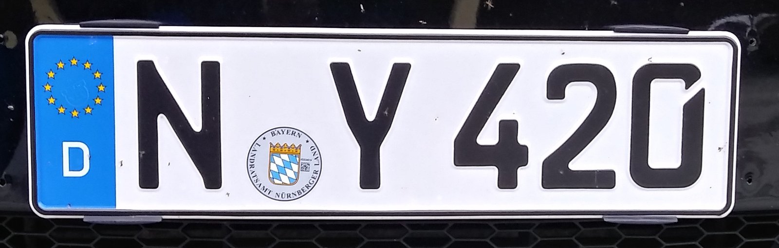 A Bavarian &ldquo;N&middot;Y 420&rdquo; German vehicle registration plate photographed at an angle, showing the black FE-Schrift lettering on white reflective plate stock with the blue EU/D band on the left.